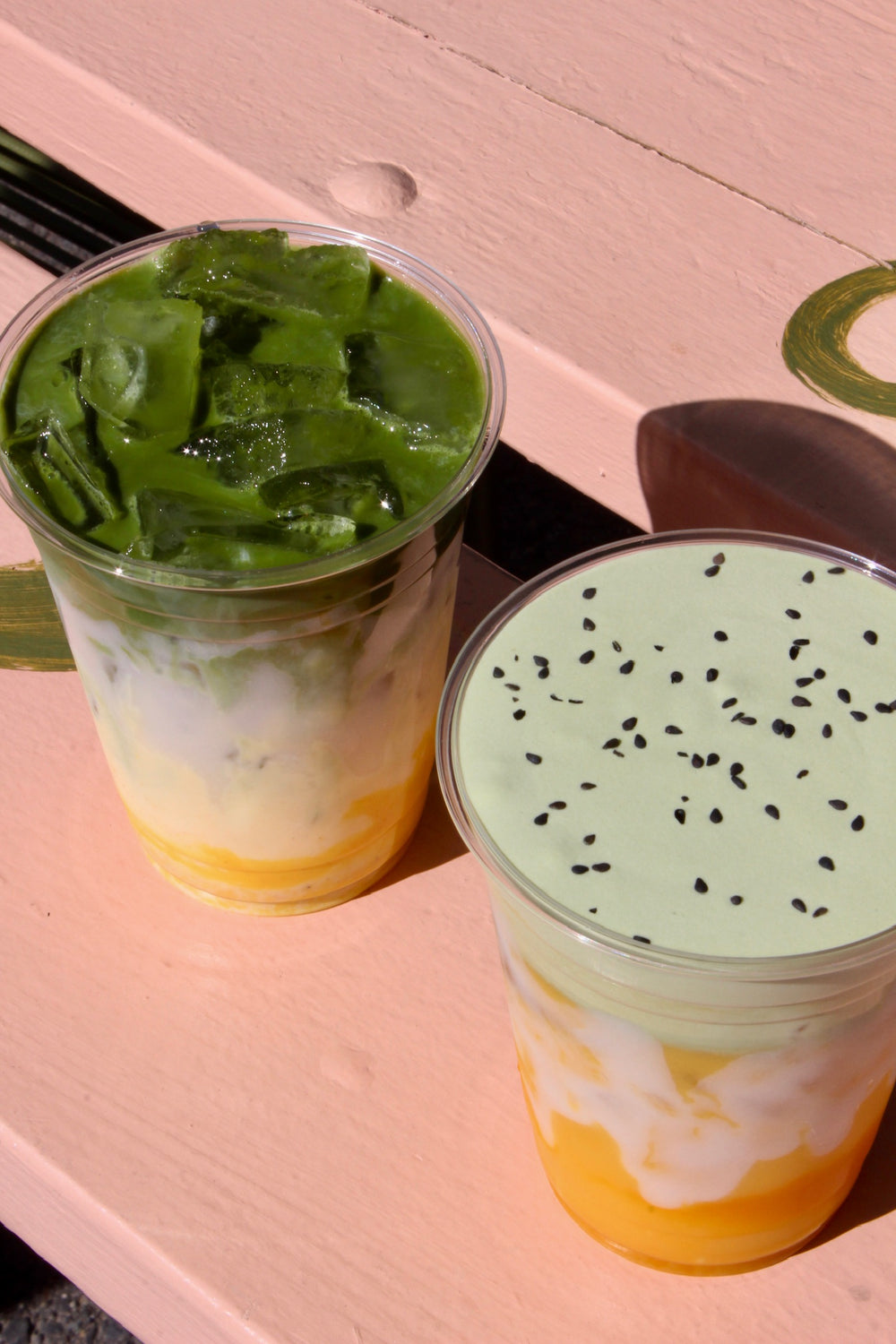 Two layered matcha drinks on a pink picnic table
