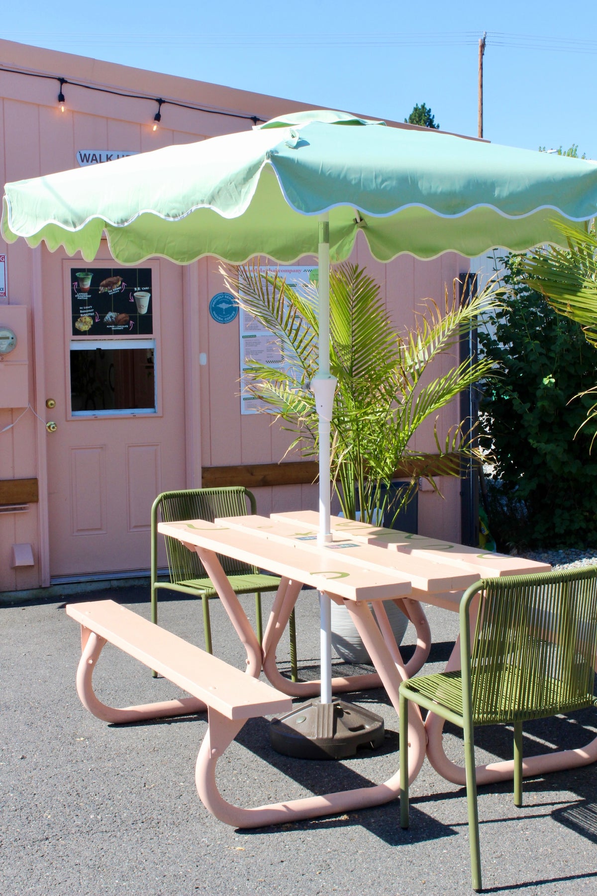 The pink Mandala Chai & Coffee Co. stand with a mint umbrella, palm and picnic table