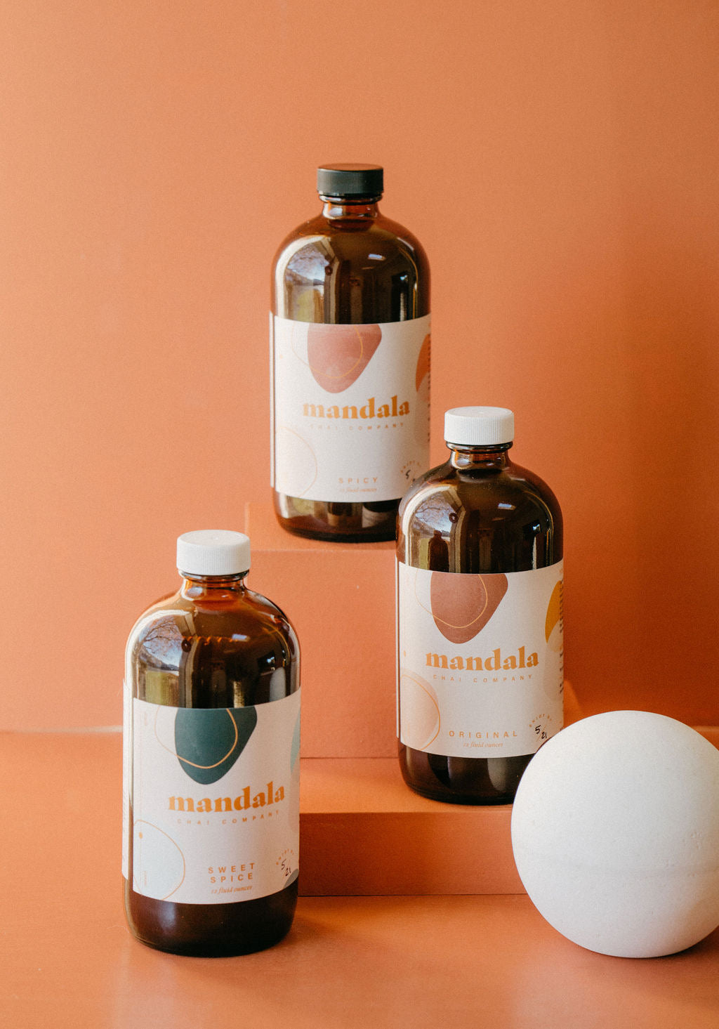 Three Mandala chai bottles on a terracotta set with dried grasses