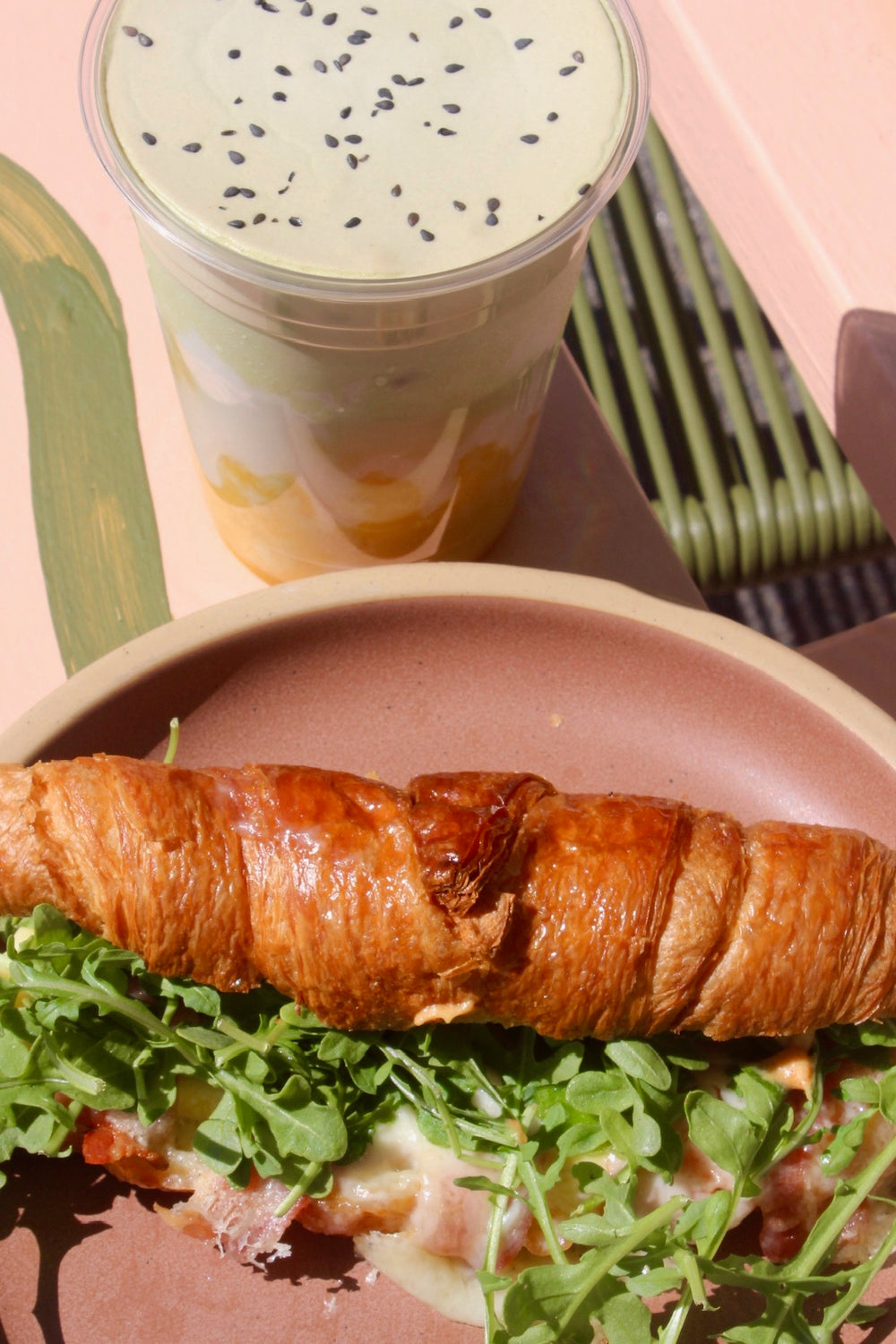 Matcha drink with black sesame beside a croissant sandwich with arugula