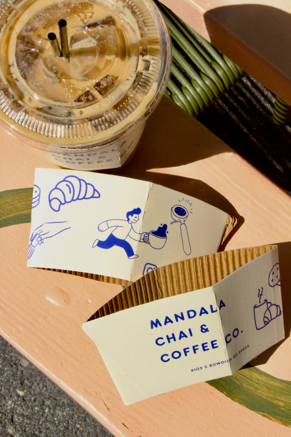 Illustrated Mandala Chai & Coffee Co. cup sleeves beside an iced coffee