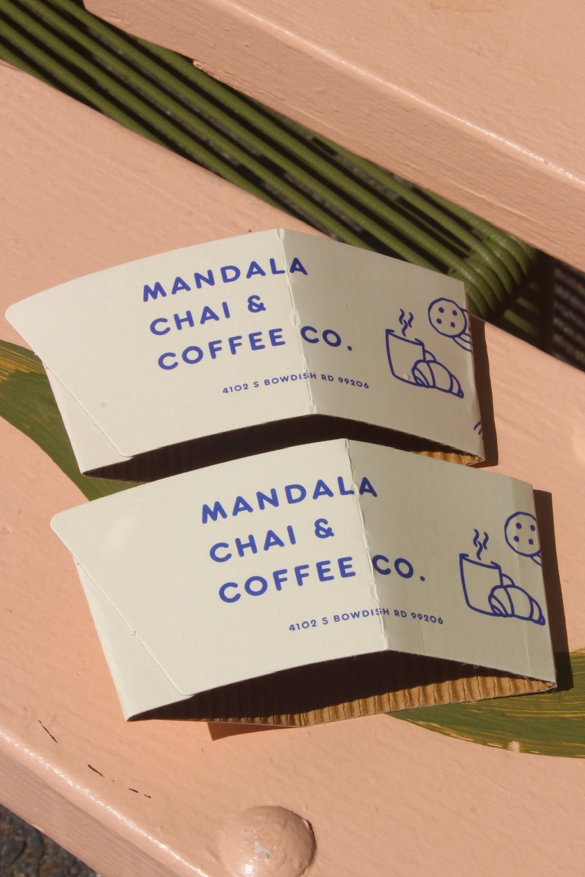 Mandala Chai & Coffee Co. cup sleeves on a pink table