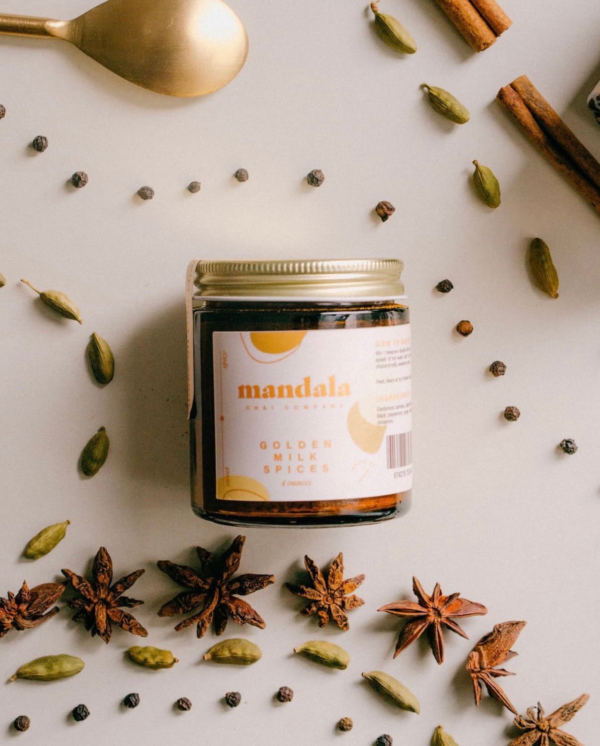 Mandala Golden Milk Spices jar surrounded by cardamom, star anise, peppercorns and cinnamon